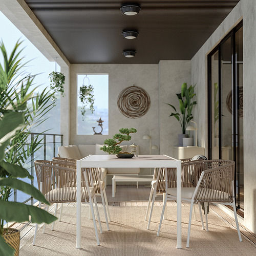 Moderno juego de comedor al aire libre con mesa de metal blanco y sillas tejidas en un patio con paredes de concreto y plantas colgantes.