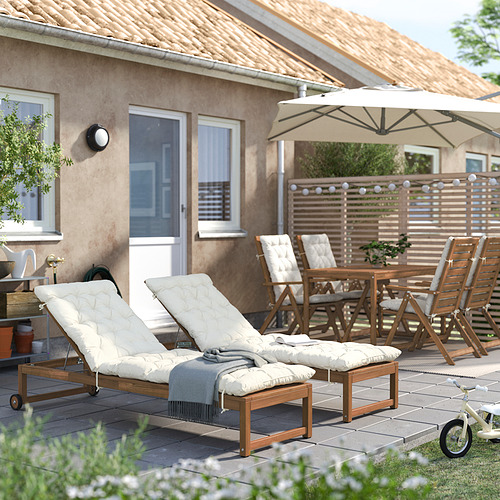 Patio trasero con sillones reclinables acolchados blancos NÄMMARÖ, mesa de madera, sillas y sombrilla grande cerca de la casa.
