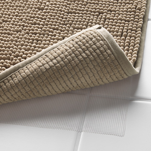 Alfombrillas de baño beige apiladas con capa de malla antideslizante debajo.
