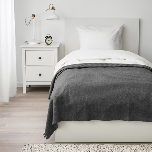 Cama con manta de vellón gris TJÄRBLOMSTER; Mesita de noche de tamaño único casi blanca con lámpara.