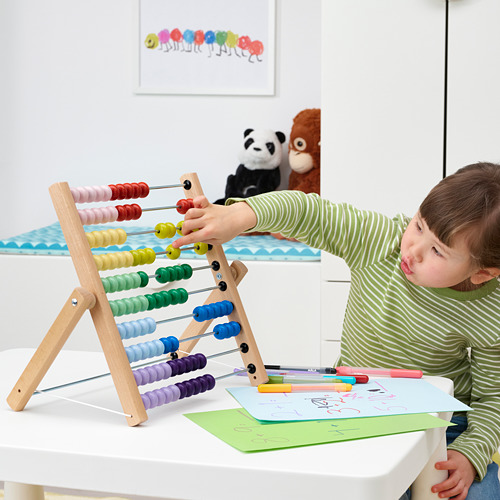 Niño jugando con ábaco de colores sobre mesa blanca; animales de peluche cerca, fomentando el aprendizaje y la diversión.
