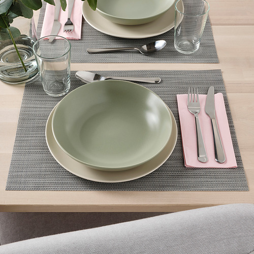 Mesa con cuenco verde, plato blanco, utensilios, vaso y servilleta sobre mantel individual.