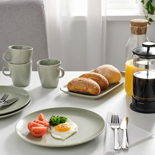 Mesa con platos de color verde claro, con comida, tazas y utensilios. La prensa francesa y la jarra con jugo están presentes.