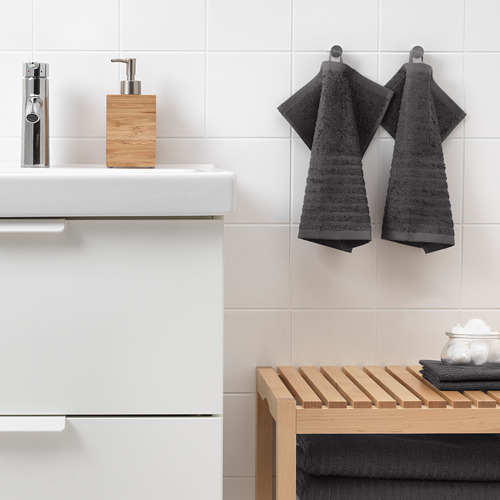 Baño moderno con lavabo blanco, grifo cromado, detalles en madera y toallas oscuras. Las toallas VÅGSJÖN cuelgan ordenadamente junto al fregadero.