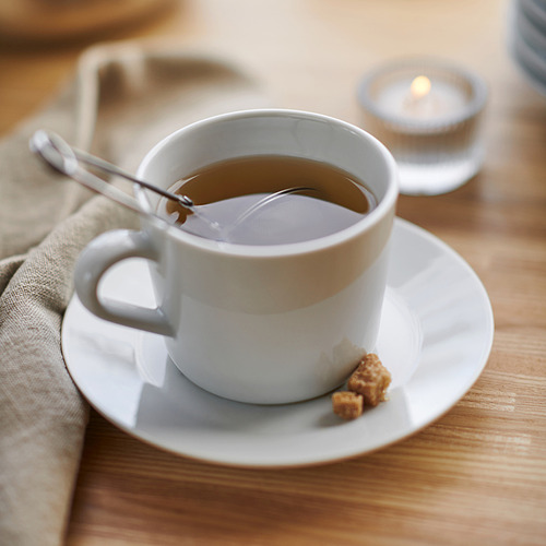 Taza de té sobre porcelana blanca, con cuchara y terrón de azúcar, colocada sobre una mesa de madera.