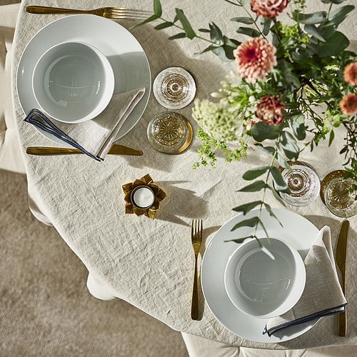 Juego de mesa con platos blancos IKEA 365+, cubiertos dorados, vasos y un centro de mesa floral.
