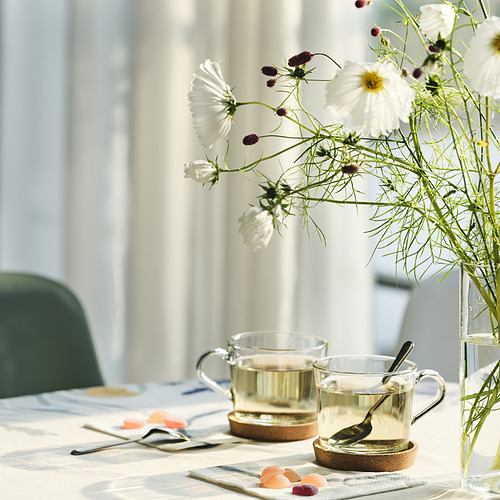 Mesa con flores blancas, dos tazas y posavasos. Los posavasos ayudan a proteger la mesa y minimizan el ruido de las tazas.