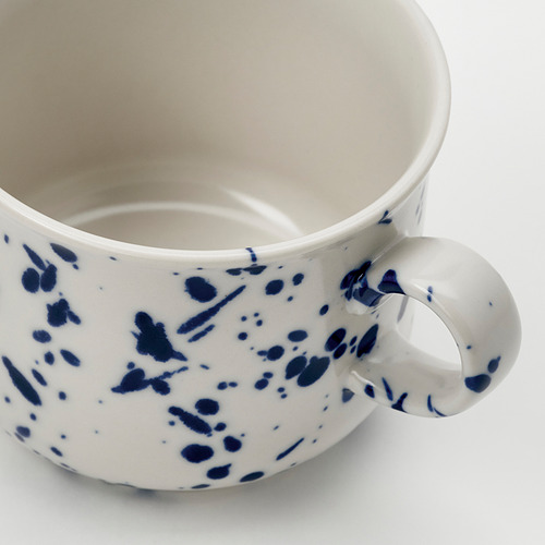 Primer plano de una taza blanca con salpicaduras azules, esmalte suave, mango resistente.