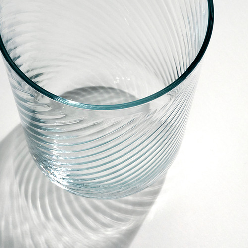 Primer plano de un vidrio elegante y transparente con un exterior liso y un interior texturizado, que proyecta sombras intrincadas, resaltando su delicada calidad.