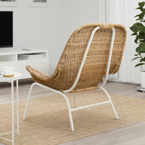 Sillón de mimbre FRYKSÅS con estructura blanca, asiento beige y respaldo sobre alfombra texturizada en un espacio minimalista.