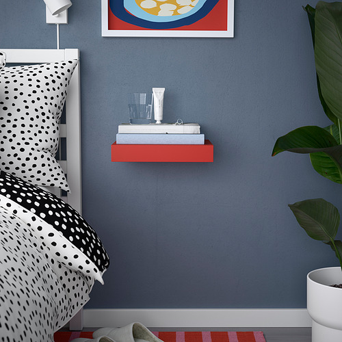 Dormitorio azul con estante rojo, ropa de cama manchada, planta y obras de arte.