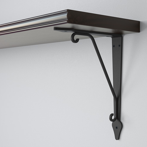 Soporte de estantería de metal oscuro con ganchos curvos fijados a la pared de color claro, que soporta una estantería de madera oscura.