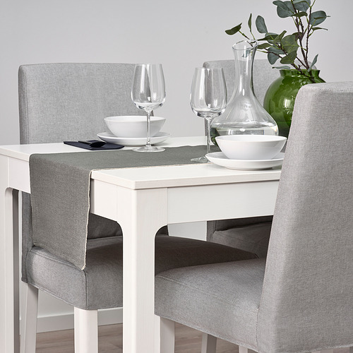 Elegante camino de mesa gris sobre mesa blanca con platos, vasos, jarrón y sillas.