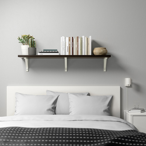 Dormitorio moderno con estante BERGSHULT montado en la pared, que exhibe libros, plantas y una canasta tejida sobre una cama blanca con almohadas grises.