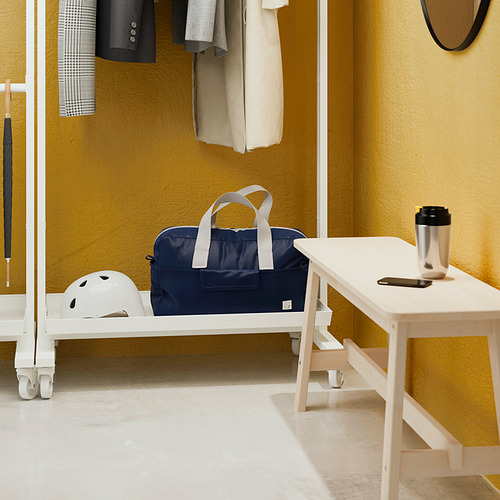 Un separador de ambientes con una barra de ropa, un estante y ruedas. Tiene capacidad para bolsos, cascos y tiene una superficie de mesa con artículos.