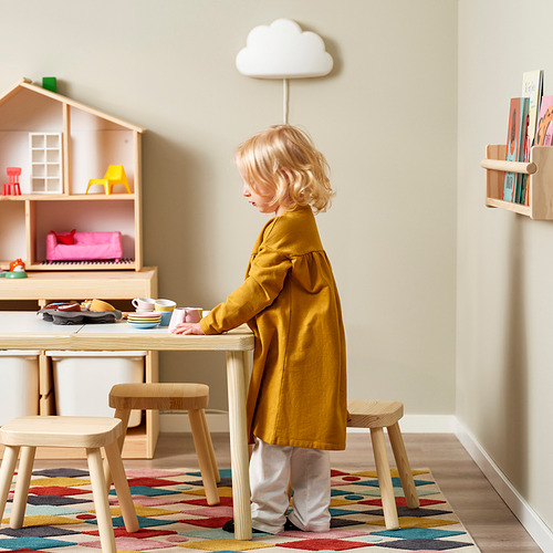 Niño jugando con juguetes de madera en la mesa. Luces y libros en la pared.