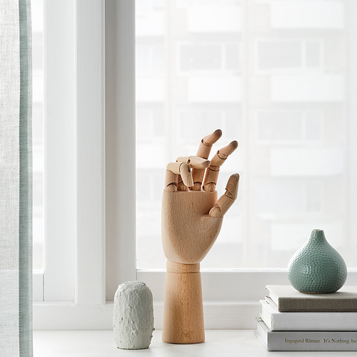 Modelo de mano de artista de madera cerca de la ventana con libros y jarrones.