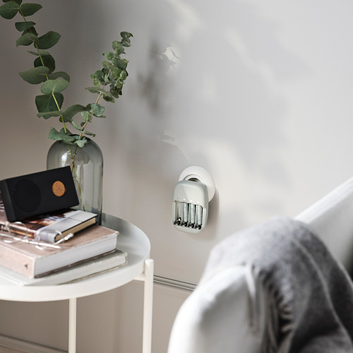 Espacio habitable minimalista con mesa auxiliar, jarrón, libros y baterías. Hombros de las personas visibles.