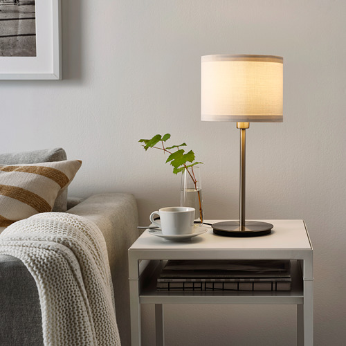 Acogedora sala de estar con sofá de almohada a rayas, lámpara cálida, taza y planta.