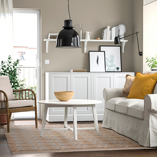 Sala de estar moderna con sofá gris, alfombra, silla de madera y mesa de centro con cuenco. La estantería contiene arte y lámpara.