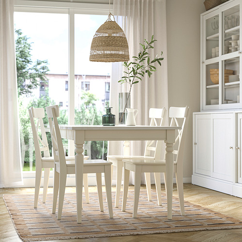 Comedor moderno con alfombra blanca TELEGRAFLINJE, mesa de madera, sillas, lámpara colgante y vitrina.
