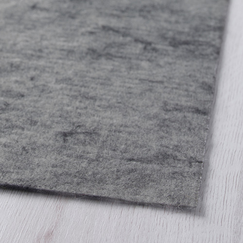 Primer plano de la base de alfombra gris, superficie suave y texturizada, doblada sobre suelo de madera.