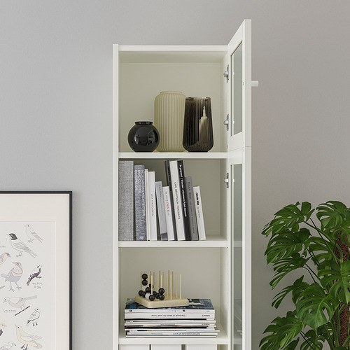 Librería blanca BILLY con puertas de cristal, guardando libros y jarrones decorativos, contra pared gris.