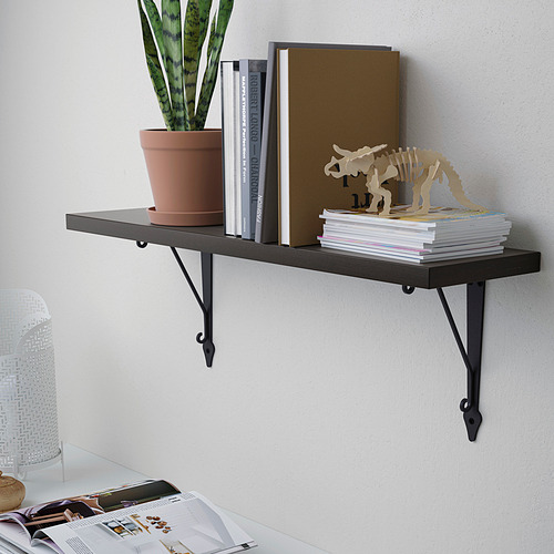 Estante montado en la pared con soportes de metal negro que sostiene libros, revistas, una planta en maceta y artículos decorativos.