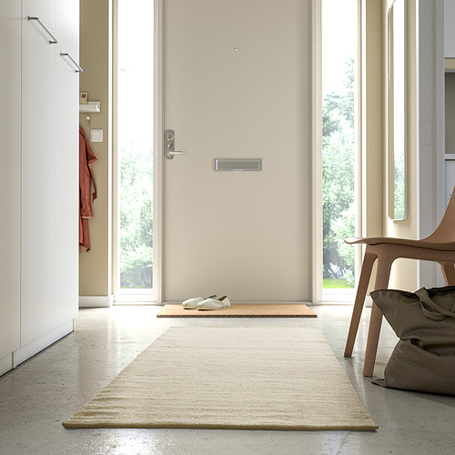 Pasillo minimalista con alfombra central beige, ligeramente más grande que el felpudo, suave y acogedor.