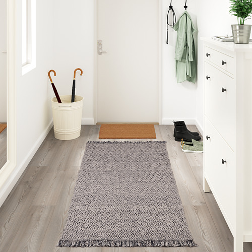 Entrada con alfombra RÖRKÄR, almacenaje blanco, botas, planta y abrigos.