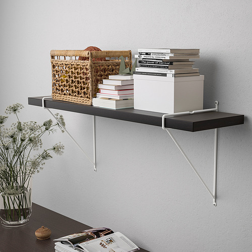 Un estante montado en la pared con soportes blancos y negros contiene cestas, libros y una caja blanca. Decorado con flores secas.