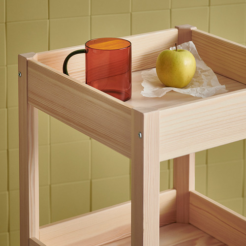 Taza SKUGGSTUBB y manzana en bandeja de madera clara. La taza de ámbar contrasta con la pared verde.