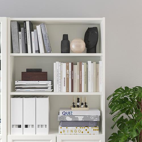 Estantería blanca BILLY con múltiples estantes que contienen libros y artículos decorativos, incluida una caja de madera, jarrones y cajas de juegos.