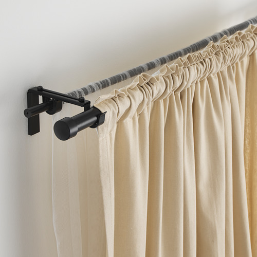 Barra de cortina ajustable de metal negro con cortinas beige, fijada a la pared, longitud y remates ajustables, carga máxima 10 kg.