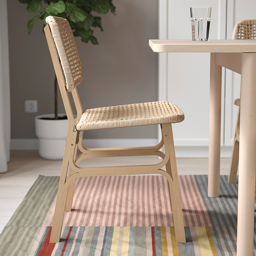 Silla con asiento y respaldo tejidos, colocada sobre alfombra a rayas cerca de la mesa del comedor.
