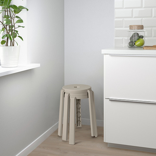 Cocina moderna con pisos de madera, gabinetes blancos y taburetes apilados. Una planta en maceta y frutas están en el mostrador.