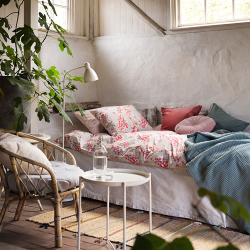 Acogedora habitación rústica con cama floral, almohadas rosas, silla de mimbre, en otros lugares, alfombra RAKLEV: colorida, mezcla tejida de yute / lana, suave, terrosa.