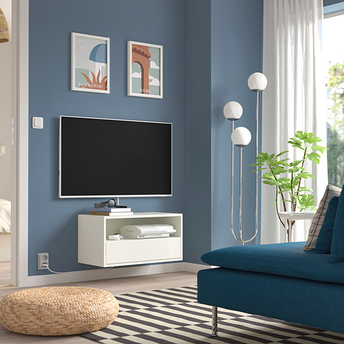 Sala de estar moderna con paredes azules, unidad de televisión EKET, sofá verde azulado, alfombra blanca y negra, lámpara de pie, planta en maceta y otomana.