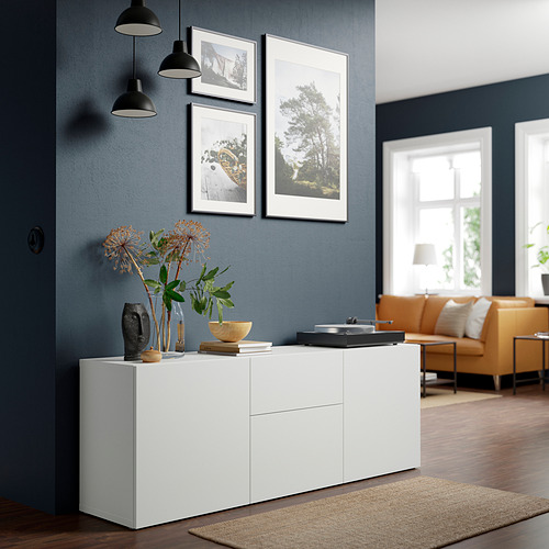 Salón moderno: aparador blanco BESTÅ, pared azul oscuro, sofá naranja, lámparas colgantes, alfombra.