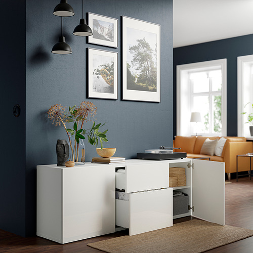 Mueble blanco BESTÅ con flores, libros, lámparas, pared azul oscuro, sofá naranja, gran ventana.
