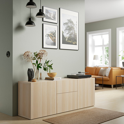Aparador BESTÅ de madera clara, elegante y minimalista, cabe debajo de cuadros colgantes, con jarrones decorativos, cerca del sofá naranja.