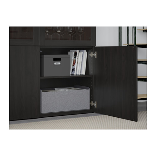 A black BESTÅ cabinet with one door open, showcasing adjustable shelves holding grey storage boxes and books.