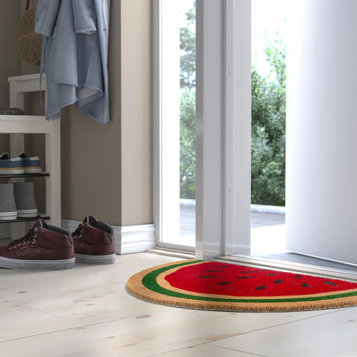 Felpudo rojo brillante en forma de sandía con cáscara verde debajo de un zapatero, cerca de un abrigo azul y una puerta.