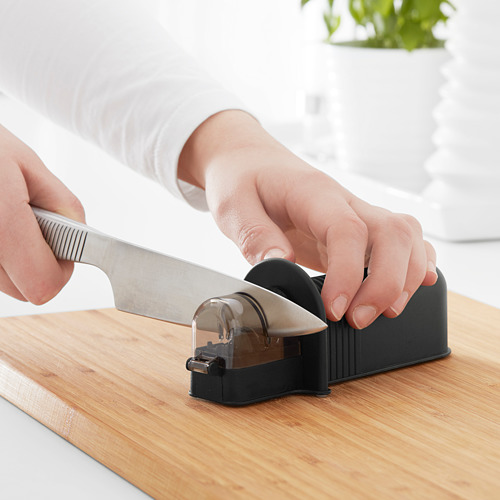 La persona afila el cuchillo en un dispositivo negro sobre una tabla de madera. Afilador de cuchillos en la cocina.