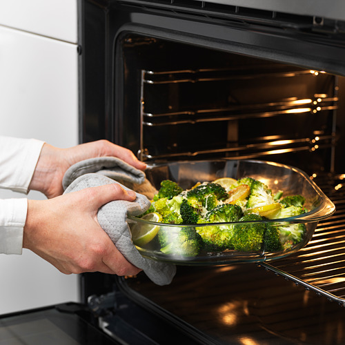 Persona colocando un plato de vidrio con brócoli en el horno. Las asas permiten una fácil elevación.