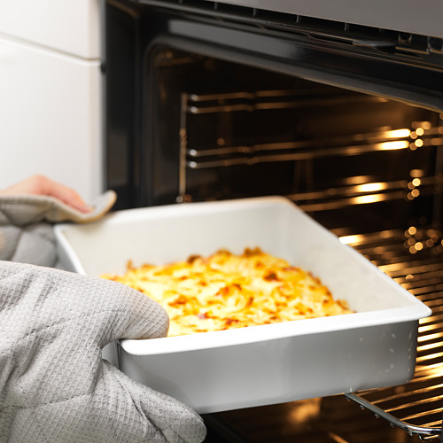 Una persona con un guante de horno saca de un horno un gran plato de cerámica blanca con comida cocinada. Las asas del plato ayudan a un manejo seguro.