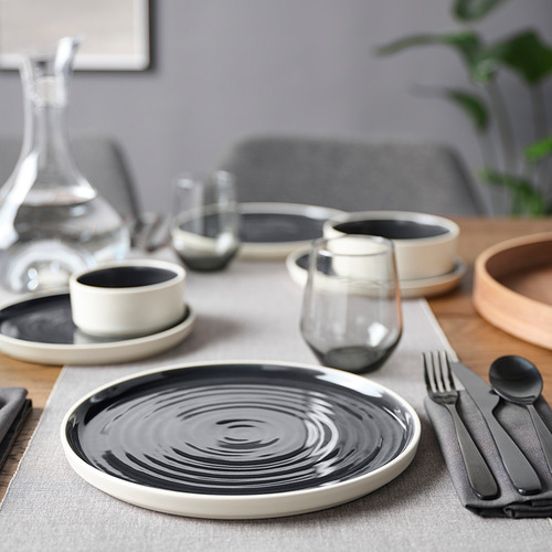 Moderna configuración de mesa OMBONAD; Platos de cerámica en blanco y negro, vasos de vidrio, cuenco de madera, cubiertos grises.