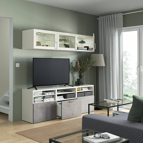 Sala de estar moderna con mueble de TV BESTÅ, TV de pantalla plana, estantes abiertos, mesa de centro con tapa de vidrio y cortinas grises junto a una gran ventana.