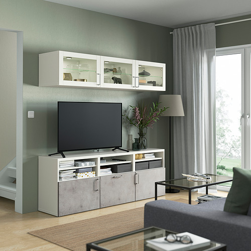 Sala de estar moderna con mueble de TV BESTÅ, vitrinas de vidrio, TV grande, mesa de café, sofá y ventana.