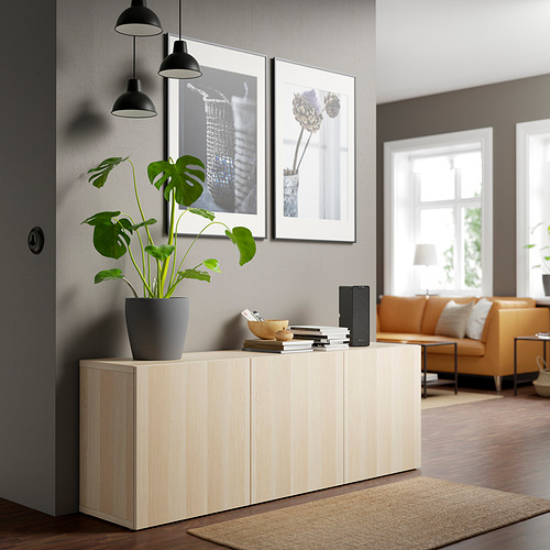 Aparador de madera BESTÅ con libros, altavoz, planta. Acogedora sala de estar con sofás y ventana.